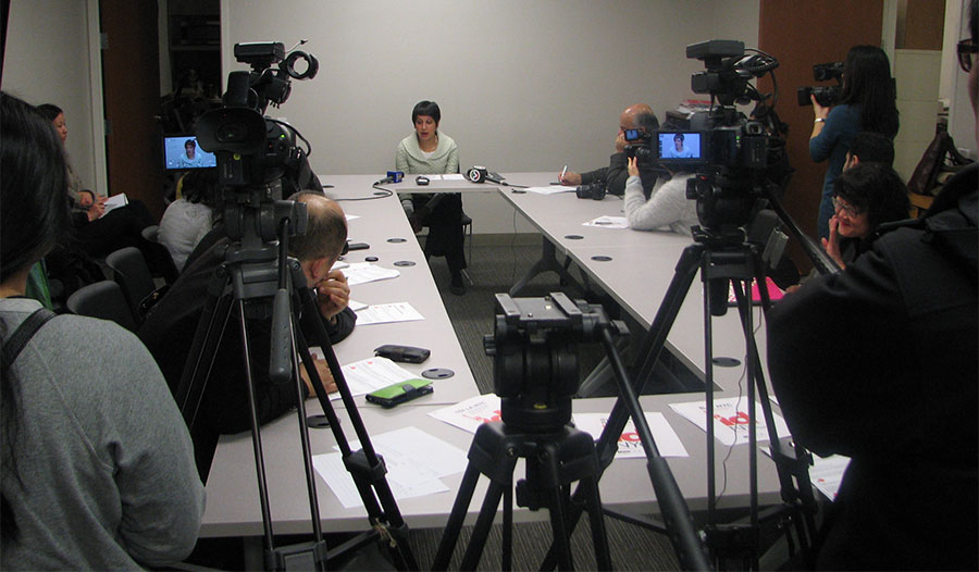 Photo of conference room filled with people and 2 cameras filming